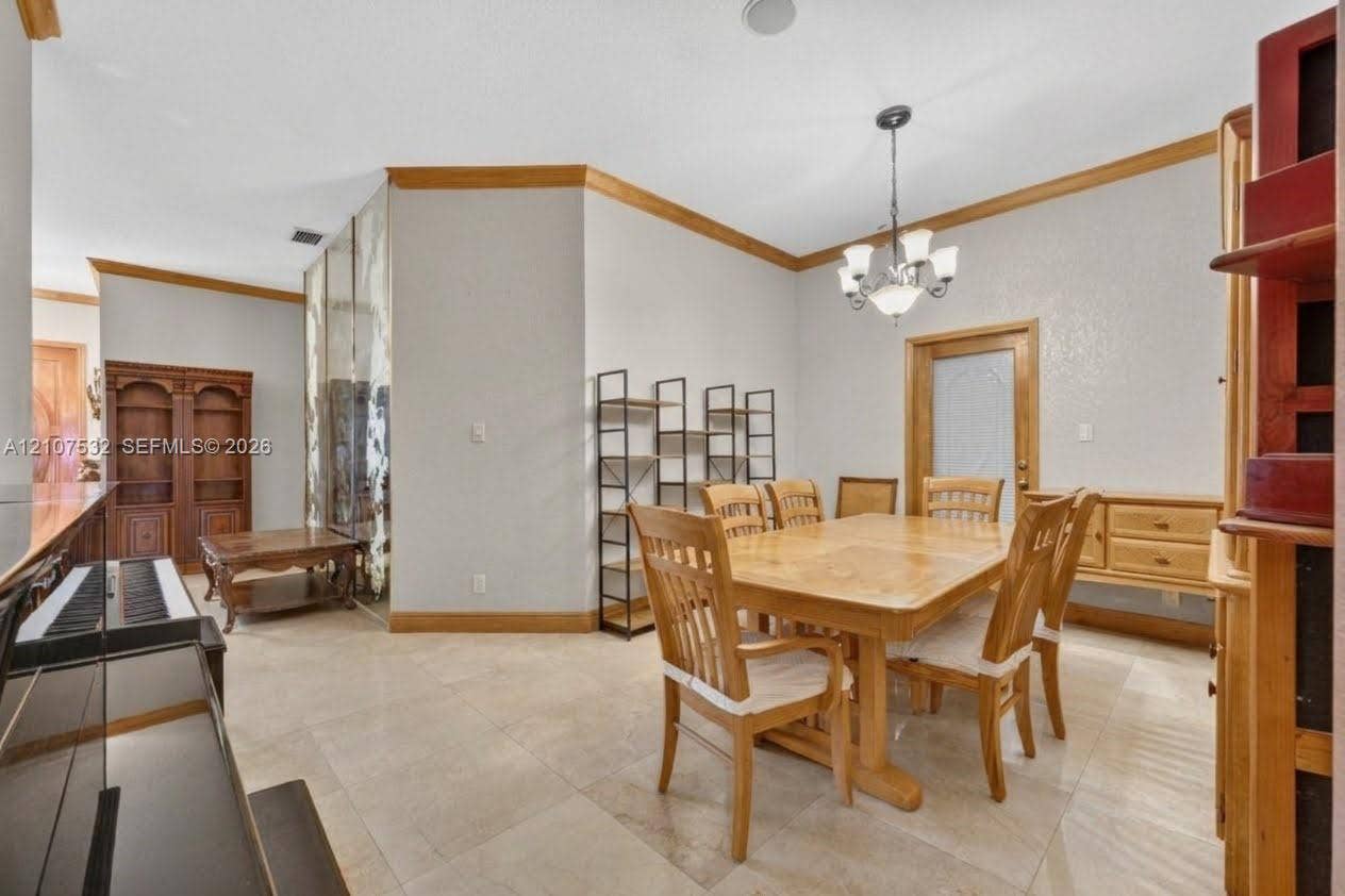 9124 NW 147th Terrace, Miami Lakes, FL 33018 Large-format stone flooring, crown molding with natural wood finish, built-in wooden cabinetry, multi-panel mirrored wall, and overhead chandelier lighting