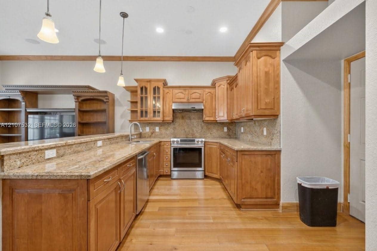 9124 NW 147th Terrace, Miami Lakes, FL 33018 Kitchen featuring custom wood cabinetry, stone countertops, stainless steel appliances, wood-finish flooring, and three pendant light fixtures