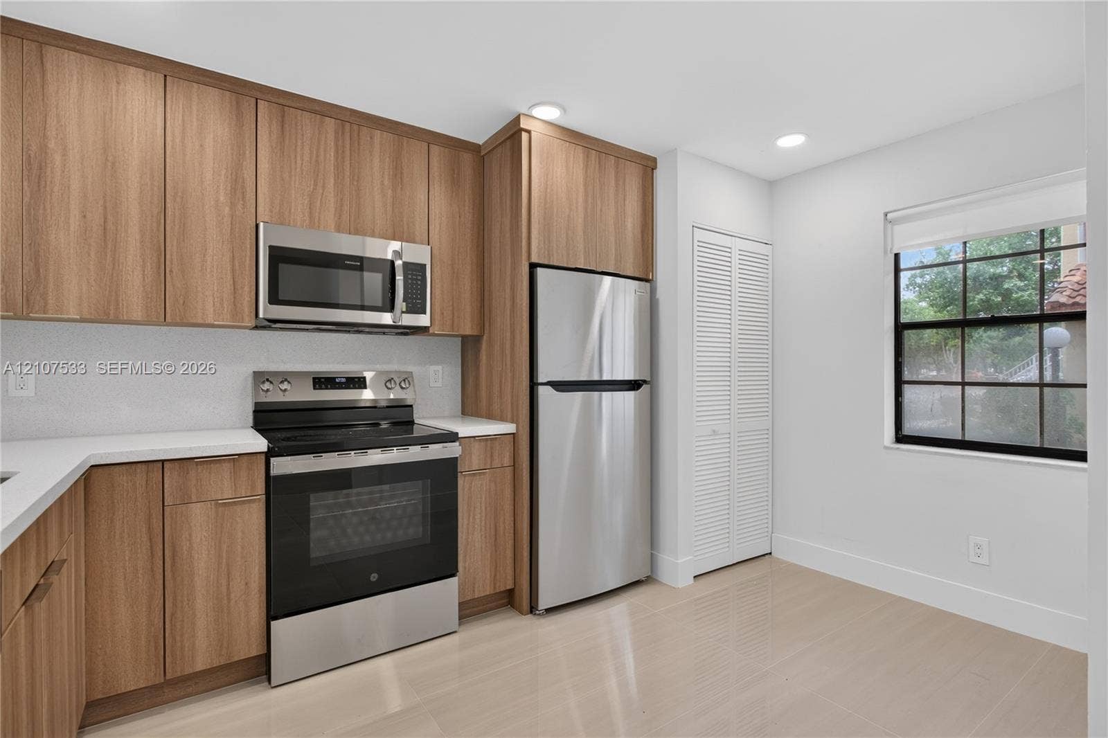 1939 Jefferson Street, #201, Hollywood, Hollywood, FL 33020 Kitchen featuring flat-panel wood-finish cabinetry, stainless steel appliances, white solid-surface countertops, tile flooring, and louvered closet doors