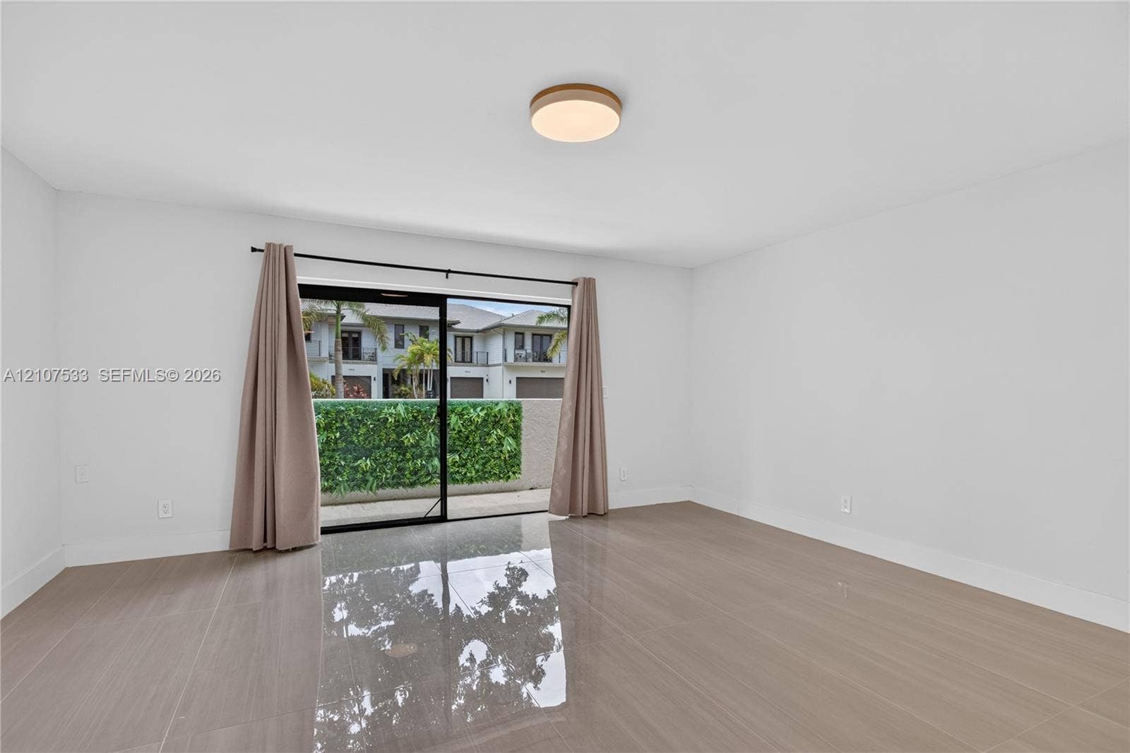 1939 Jefferson Street, #201, Hollywood, Hollywood, FL 33020 Interior space featuring large-format tile flooring, a circular flush-mount ceiling light, and sliding glass doors opening to a concrete patio with perimeter greenery