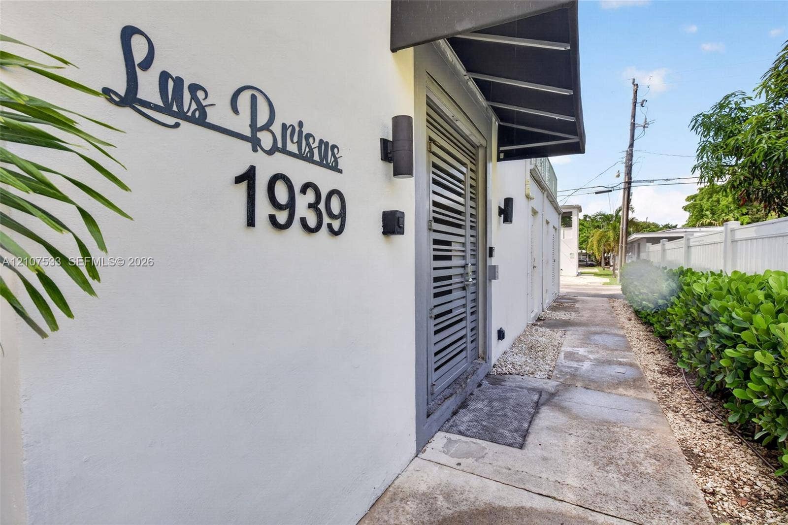 1939 Jefferson Street, #201, Hollywood, Hollywood, FL 33020 Exterior facade featuring smooth stucco finish, custom metal address signage, wall-mounted cylindrical sconces, dark metal awning, and louvered entry door