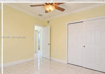 Room featuring light-toned tile flooring, white six-panel closet doors, crown molding, and a ceiling fan with integrated lighting