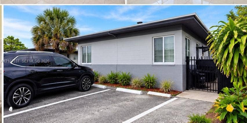 Two-tone painted masonry exterior featuring designated paved parking, sliding windows, and a black metal gated entryway
