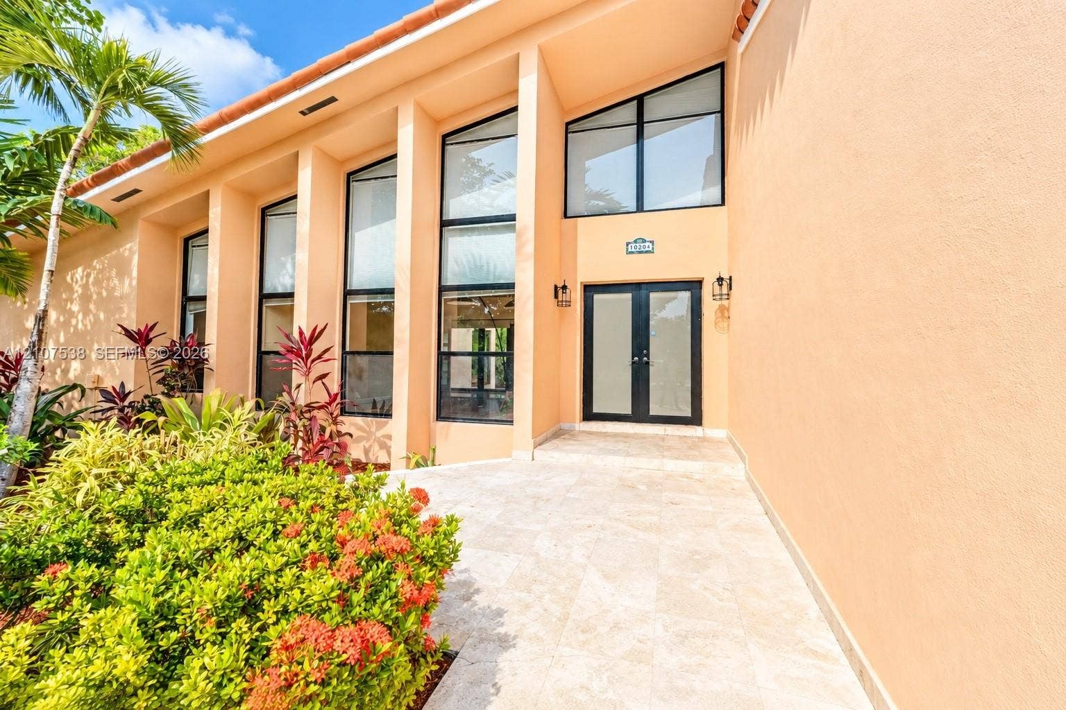10204 SW 96th Court, Miami, Miami, FL 33176 Stucco exterior featuring soaring multi-pane windows, double entry doors, and expansive stone-finish patio flooring