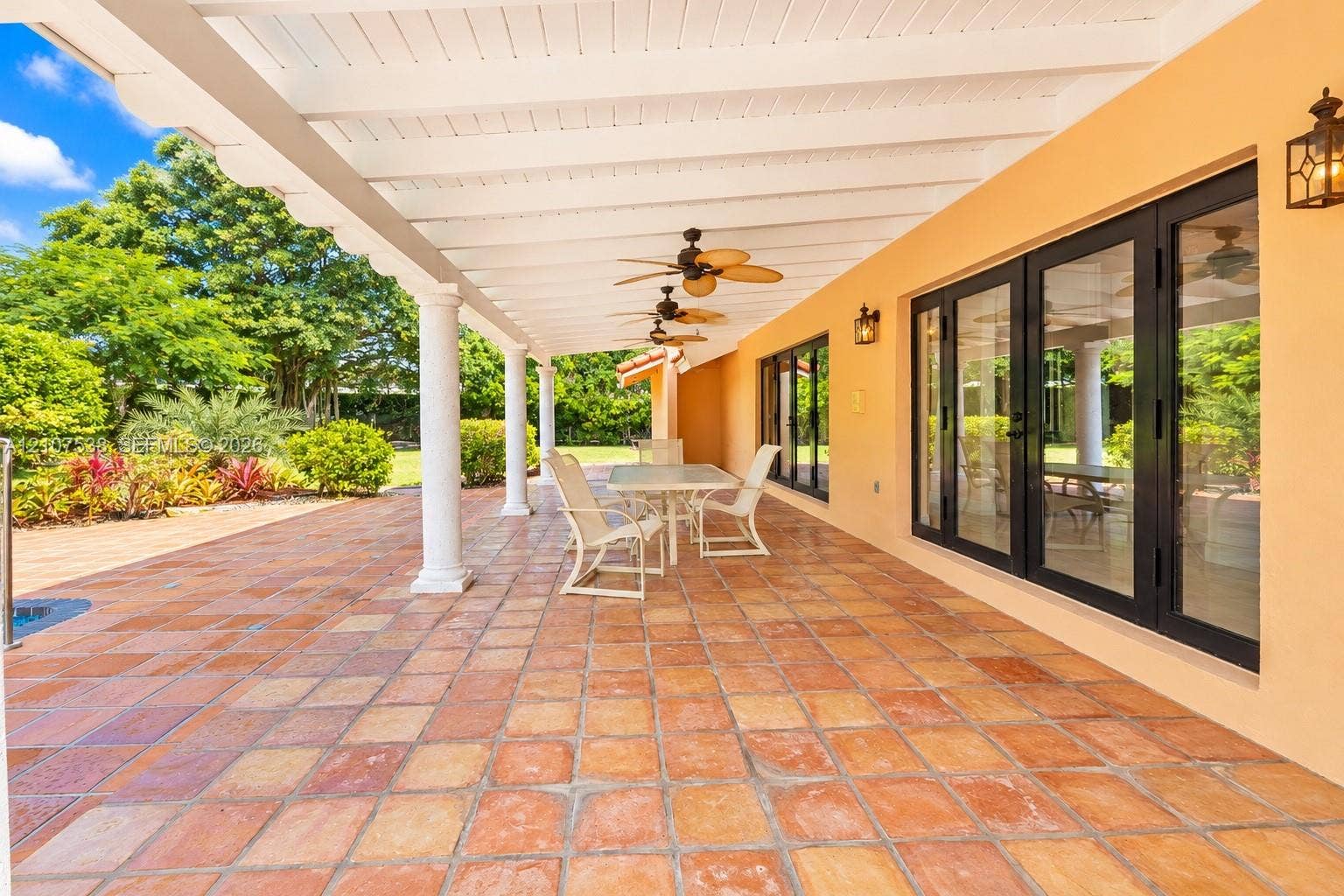 10204 SW 96th Court, Miami, Miami, FL 33176 Covered lanai featuring terracotta-tile flooring, white structural columns, ceiling-mounted fans, and black-framed multi-panel glass doors