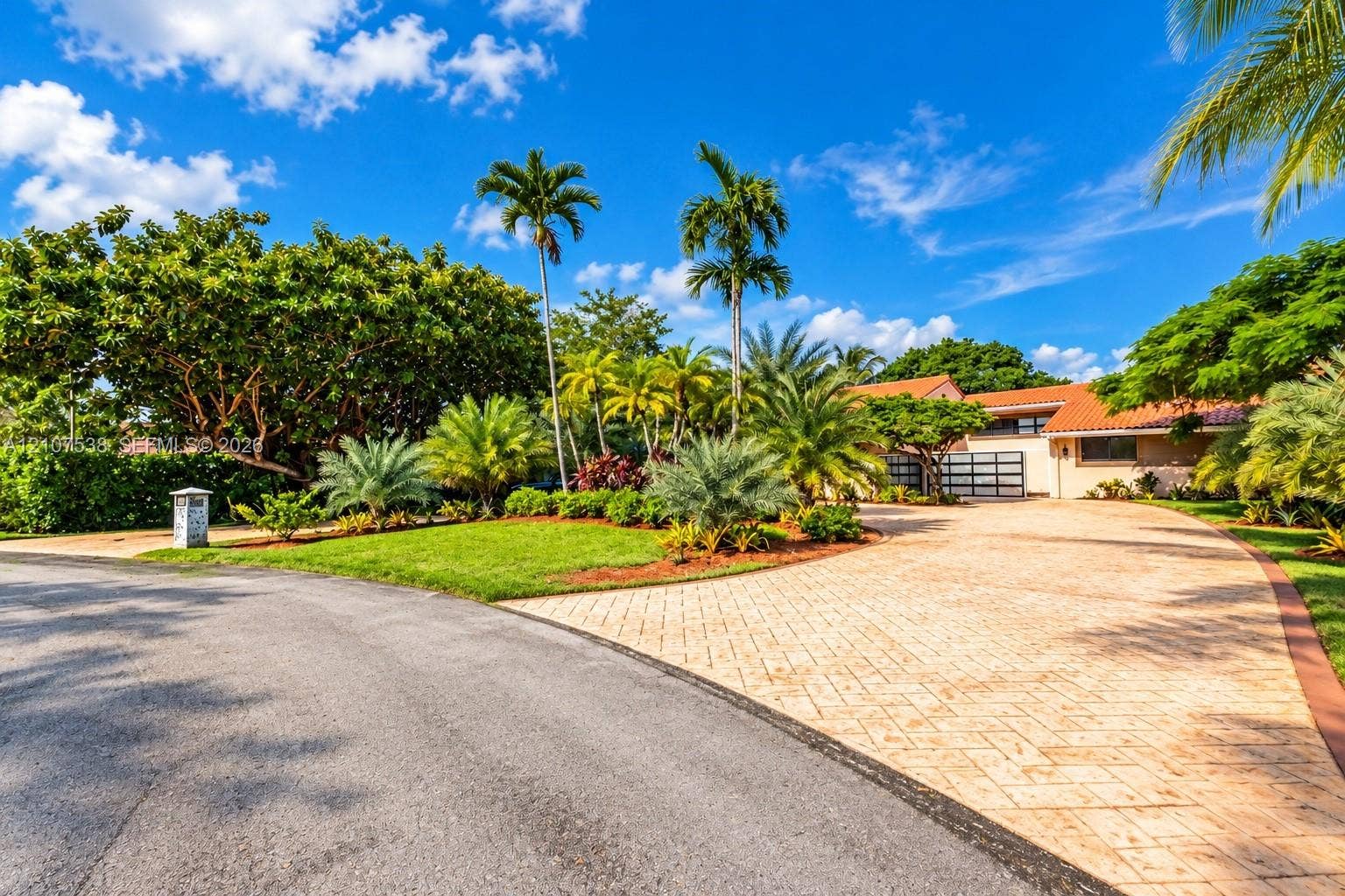 10204 SW 96th Court, Miami, Miami, FL 33176 Single-story residence featuring a tile roof, expansive paver driveway, multi-panel garage door, and mature tropical landscaping