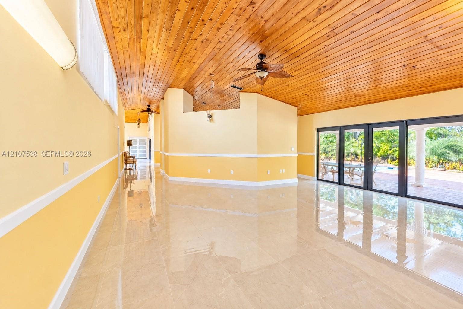 10204 SW 96th Court, Miami, Miami, FL 33176 Spacious interior featuring a wood-plank vaulted ceiling, polished stone flooring, chair rail molding, and multi-panel glass doors