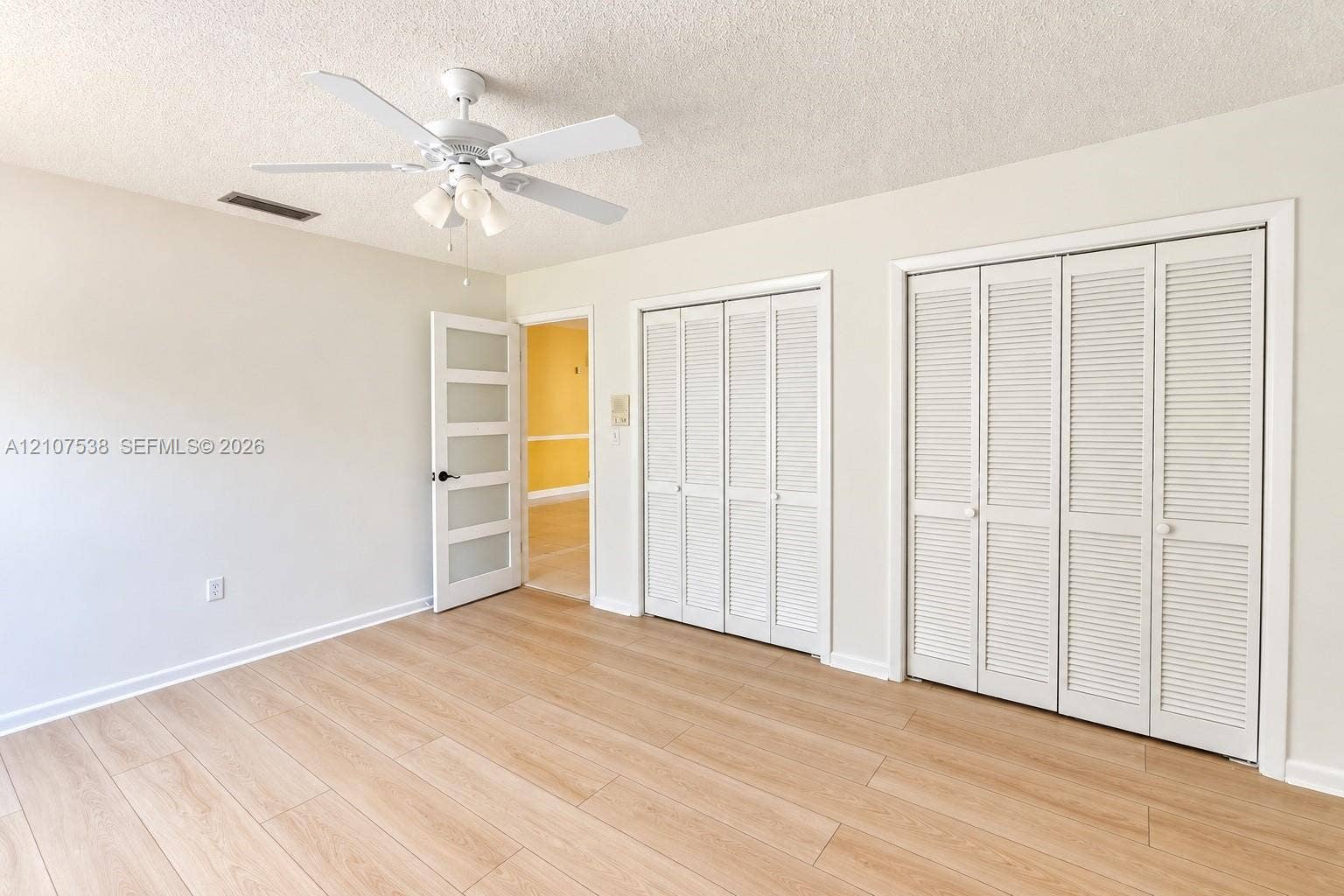 10204 SW 96th Court, Miami, Miami, FL 33176 Room featuring wood-finish flooring, dual closets with louvered doors, a five-panel frosted glass door, and an overhead ceiling fan with integrated lighting