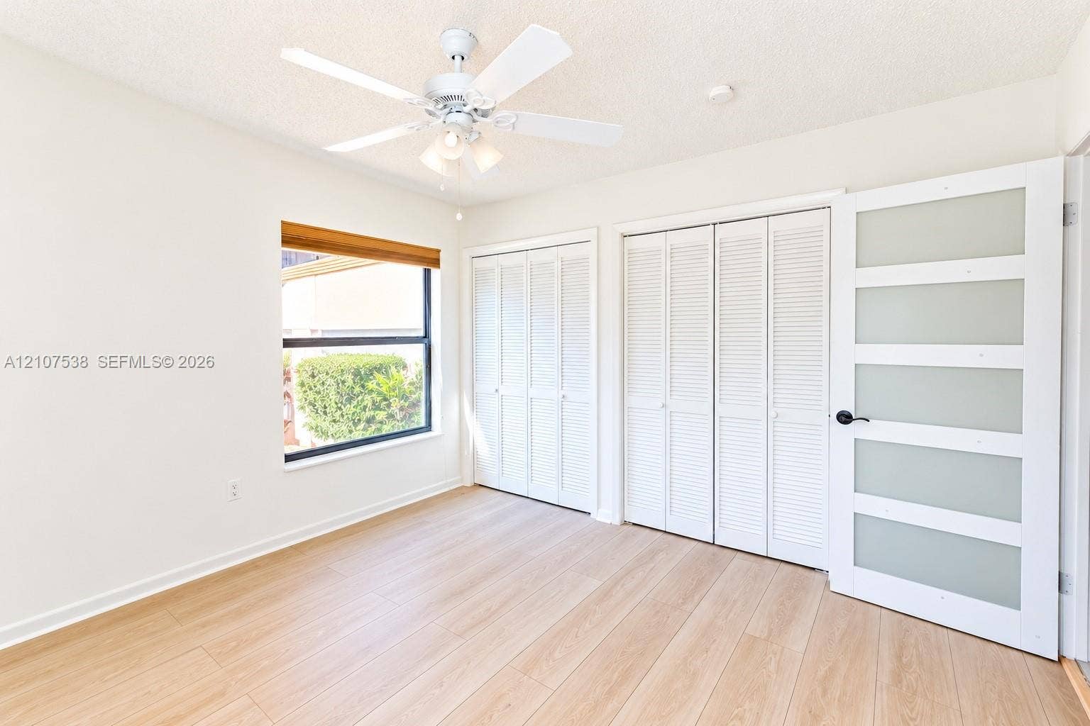 10204 SW 96th Court, Miami, Miami, FL 33176 Room featuring wood-finish flooring, dual bi-fold louvered closets, a frosted glass paneled door, and a ceiling fan with integrated light fixture
