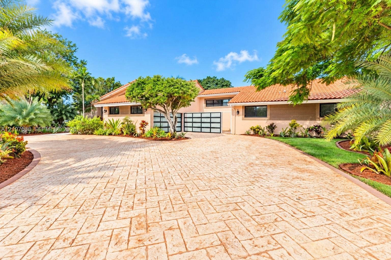 10204 SW 96th Court, Miami, Miami, FL 33176 Stamped concrete driveway featuring a herringbone pattern, terracotta roof tiles, and modern garage doors with frosted glass panels, accented by mature palm trees and manicured landscaping