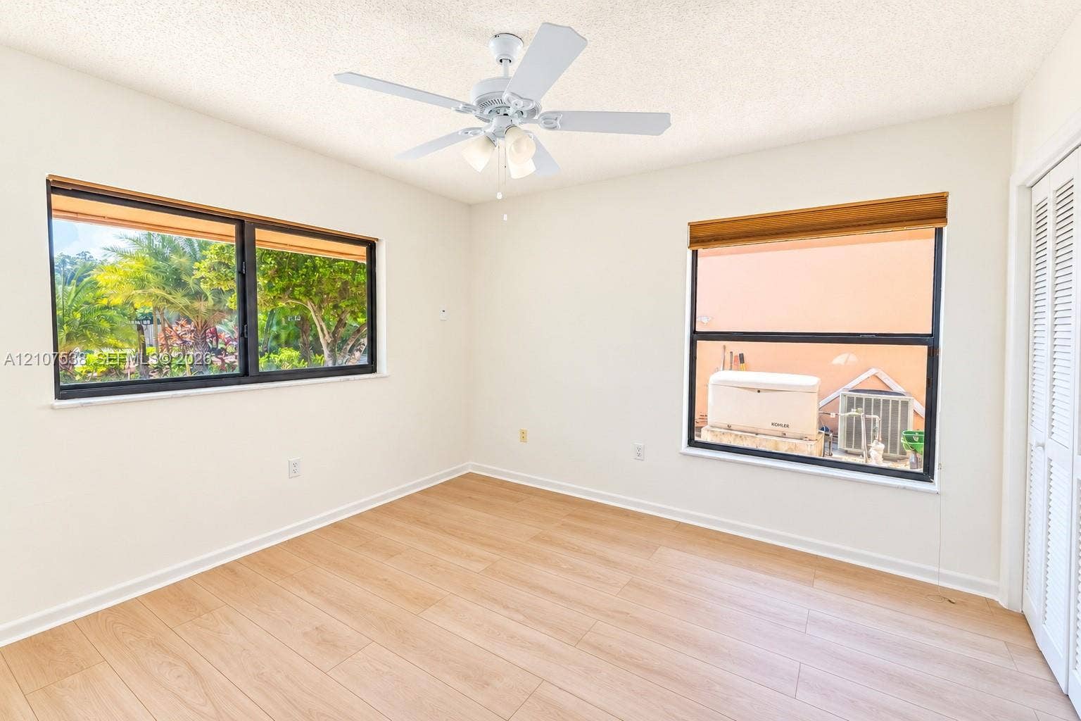 10204 SW 96th Court, Miami, Miami, FL 33176 Interior space featuring light-toned wood-finish flooring, dual windows with black frames, white louvered closet doors, and a ceiling fan with integrated lighting