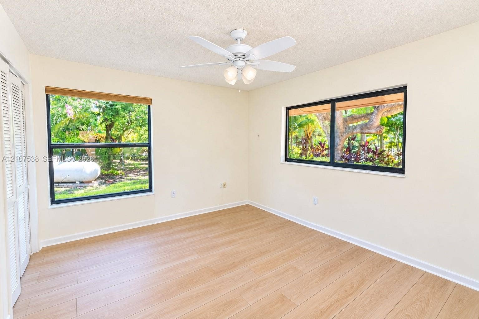 10204 SW 96th Court, Miami, Miami, FL 33176 Room featuring wood-finish flooring, dual windows with dark frames, white louvered closet doors, and a ceiling fan with integrated light fixture