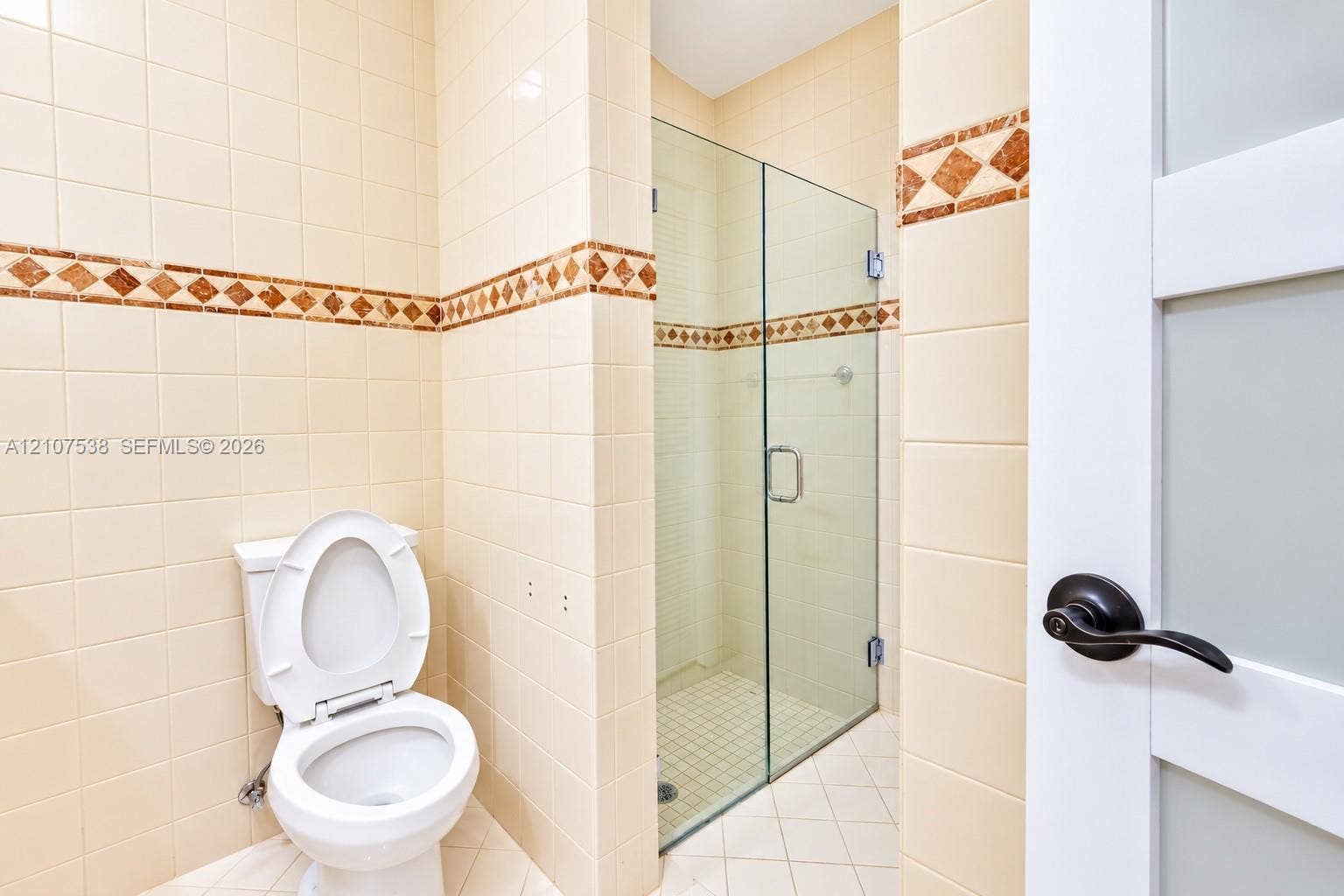 10204 SW 96th Court, Miami, Miami, FL 33176 Bathroom featuring full-height ceramic wall tiling with decorative accent inlay, a glass-enclosed shower, and a white door with frosted glass panels and matte black hardware