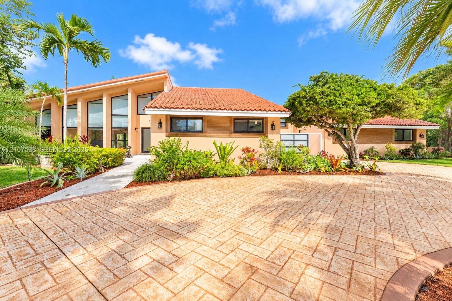 10204 SW 96th Court, Miami, Miami, FL 33176 Stucco exterior featuring a terracotta tile roof, expansive floor-to-ceiling windows, patterned paver driveway, and mature tropical landscaping