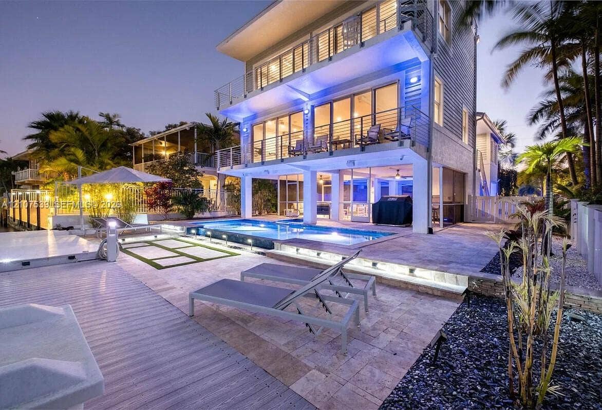 20 Center Lane, Key Largo, FL 33037 Multi-story coastal residence featuring a stone-paved pool deck, elevated balconies with metal railings, a swimming pool with integrated lighting, and tiered hardscaping