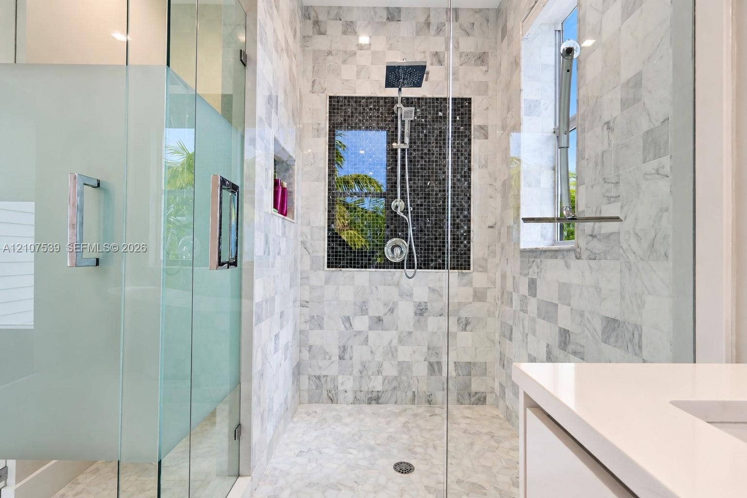 20 Center Lane, Key Largo, FL 33037 Walk-in shower featuring glass paneling, floor-to-ceiling stone-tiled walls, a mosaic accent inlay, a wall-mounted shower system, and a built-in recessed shelving niche