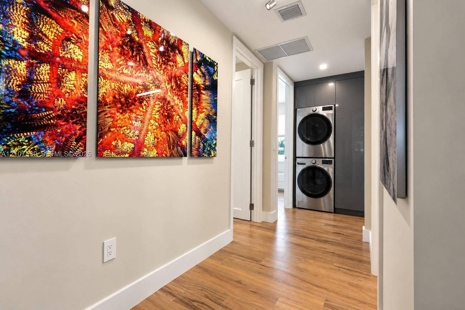 20 Center Lane, Key Largo, FL 33037 Laundry area featuring a stainless steel stacked washer and dryer unit, floor-to-ceiling charcoal gray cabinetry, and wood-finish flooring