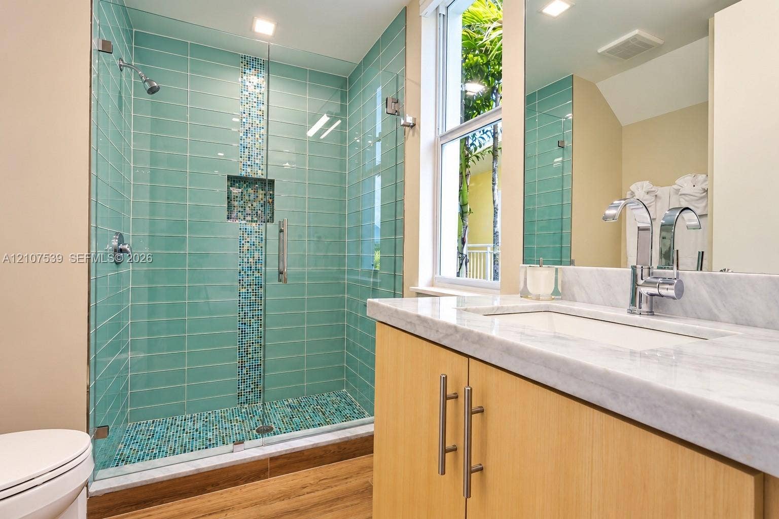 20 Center Lane, Key Largo, FL 33037 Walk-in shower with horizontal tile surround, mosaic accent strip, and glass enclosure, paired with a vanity featuring a light stone countertop, an integrated rectangular sink, and chrome fixtures