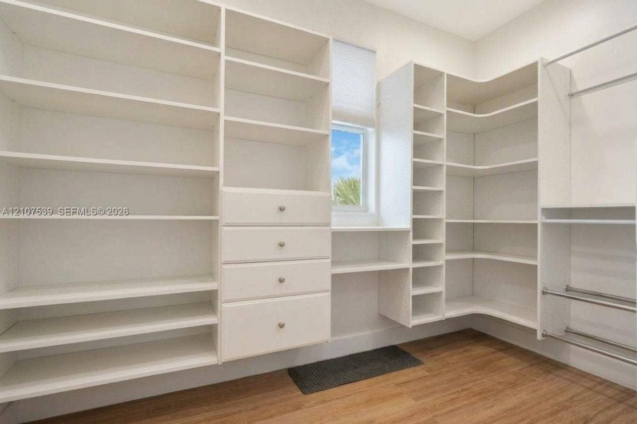 20 Center Lane, Key Largo, FL 33037 Custom white built-in shelving featuring floor-to-ceiling storage, integrated drawer units with metallic hardware, corner shelving, and metal hanging rods over wood-finish flooring