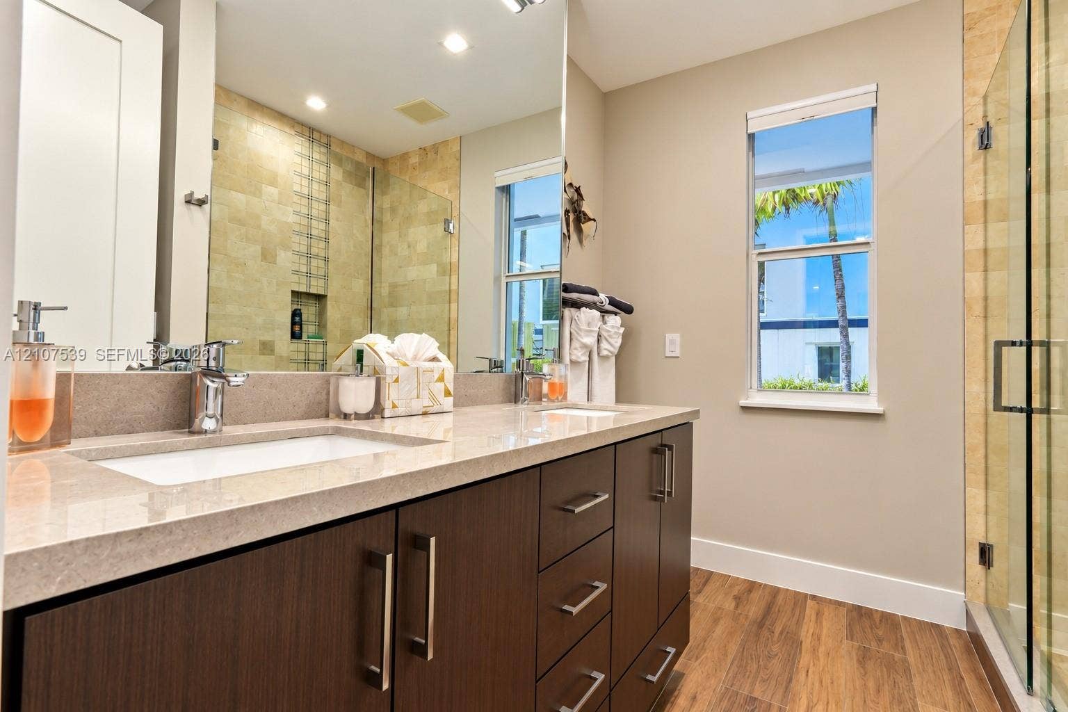 20 Center Lane, Key Largo, FL 33037 Dual-sink vanity with composite countertop, cabinetry with metallic hardware, wood-finish flooring, and a glass-enclosed shower with tiled wall accents