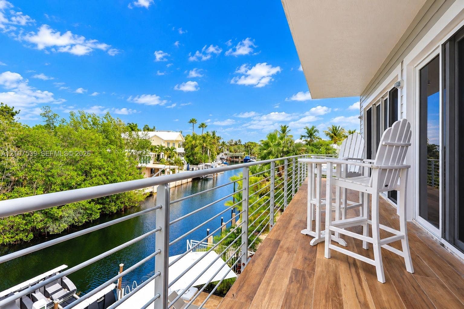 20 Center Lane, Key Largo, FL 33037 Covered balcony featuring wood-finish flooring, metal cable railing, and sliding glass door access, overlooking a canal and mature landscaping