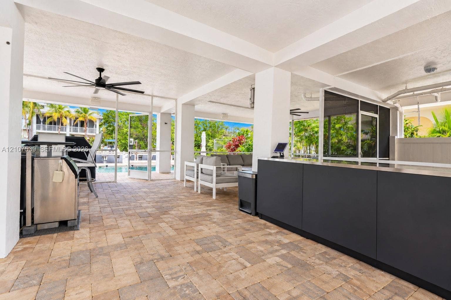 20 Center Lane, Key Largo, FL 33037 Covered patio featuring paver flooring, an outdoor kitchen with matte dark cabinetry, a built-in stainless steel grill, and a ceiling-mounted fan