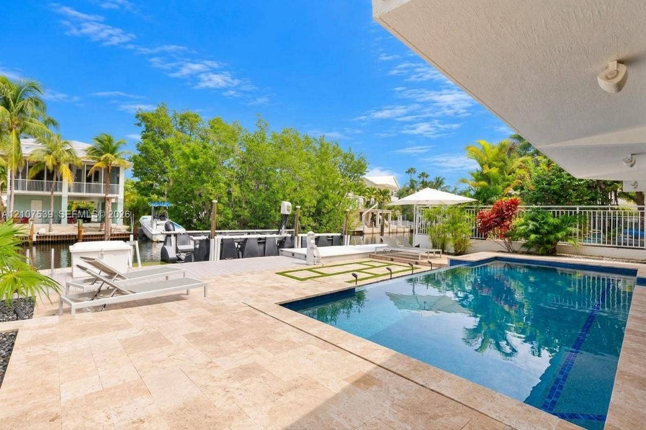 20 Center Lane, Key Largo, FL 33037 Waterfront pool deck featuring stone-finish pavers, integrated swimming pool, private boat dock, and canal frontage