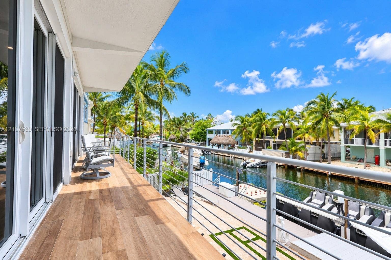 20 Center Lane, Key Largo, FL 33037 Covered balcony featuring wood-finish flooring, stainless steel cable railing, and sliding glass door access, overlooking a canal