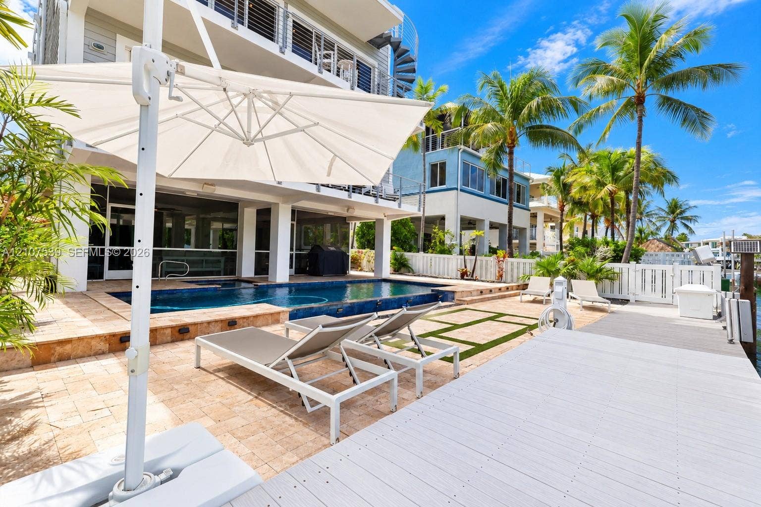 20 Center Lane, Key Largo, FL 33037 Outdoor living area featuring a swimming pool, stone-finish paver patio, composite dock, and a spiral exterior staircase