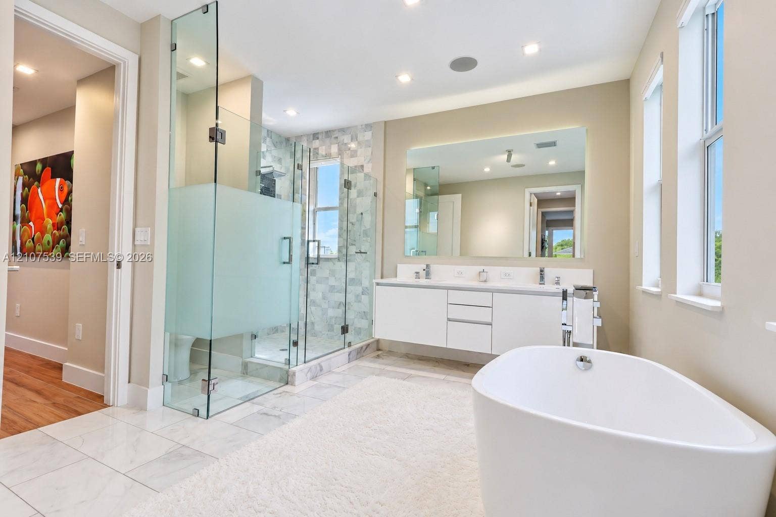 20 Center Lane, Key Largo, FL 33037 Freestanding soaking tub, glass-enclosed shower with tiled surround, and floating dual-sink vanity with a large wall-mounted mirror