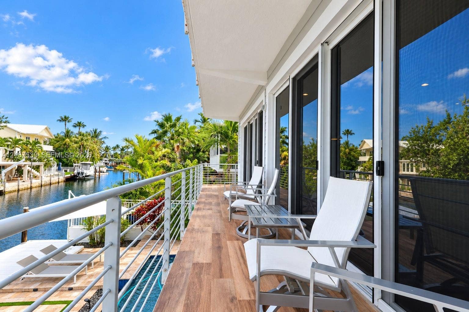 20 Center Lane, Key Largo, FL 33037 Waterfront balcony featuring wood-finish flooring, a horizontal cable railing system, and multiple floor-to-ceiling glass sliding doors