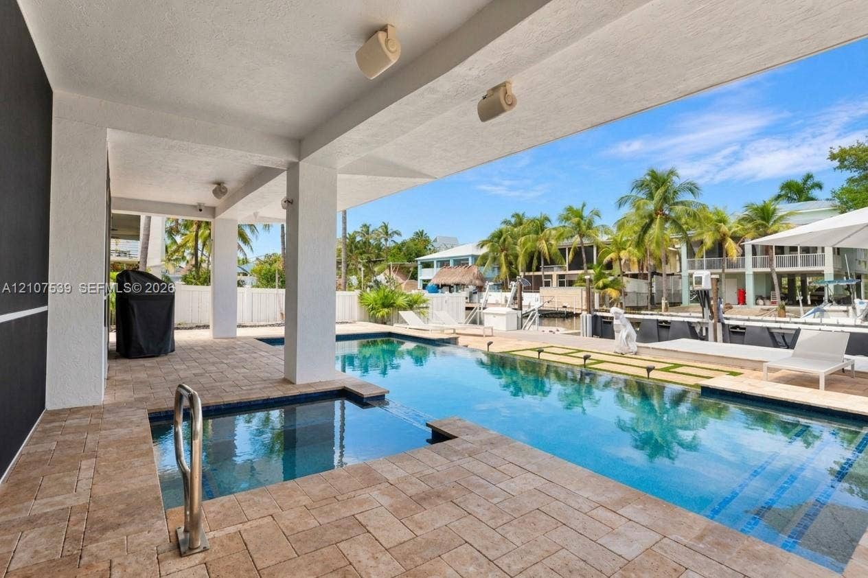 20 Center Lane, Key Largo, FL 33037 Covered lanai with stone-paver decking, swimming pool featuring an integrated spa, and concrete bulkhead leading to a waterway