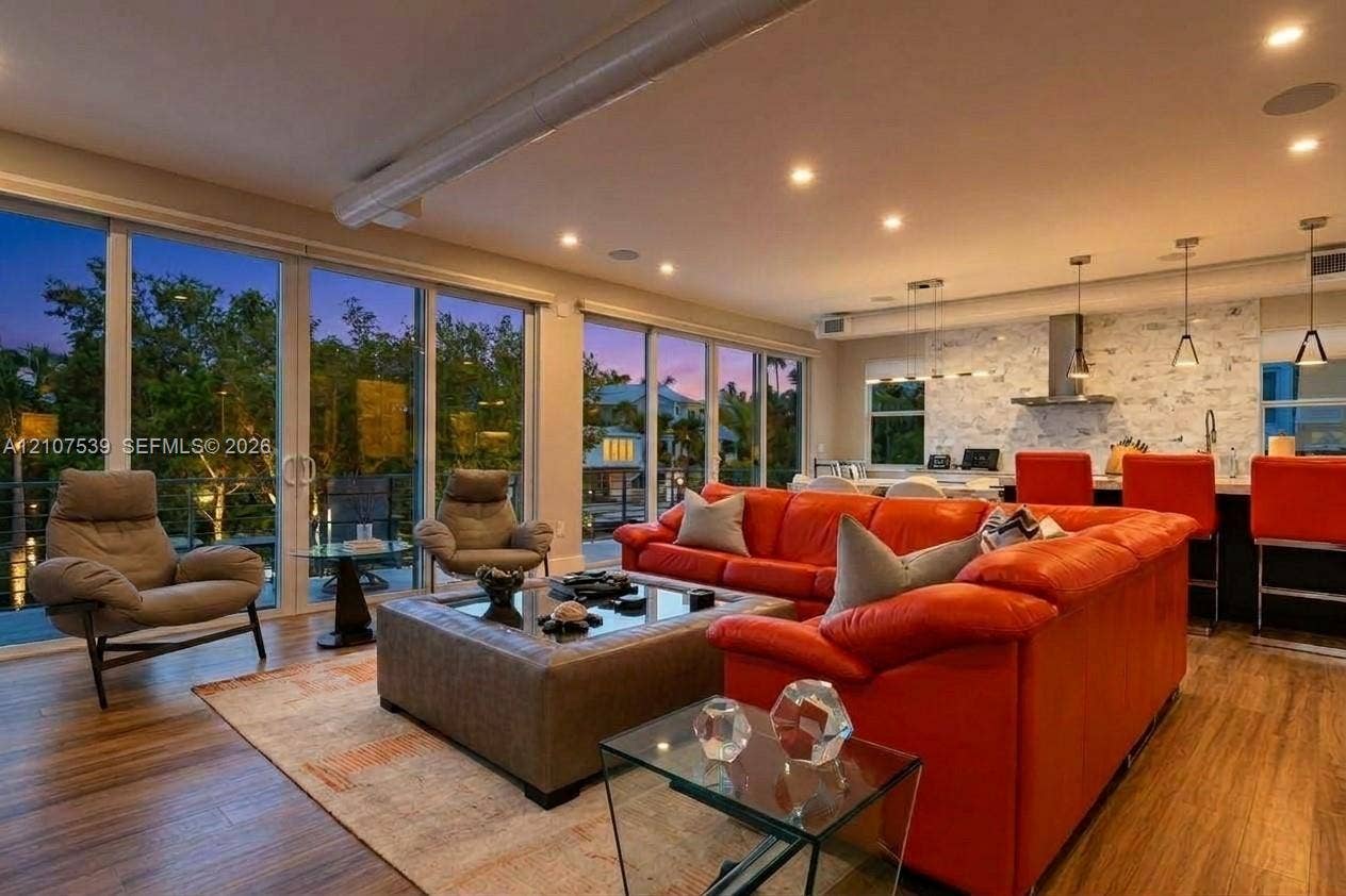 20 Center Lane, Key Largo, FL 33037 Open-concept living space featuring expansive floor-to-ceiling glass doors, wood-finish flooring, recessed lighting, and kitchen backsplash with stone-finish cladding