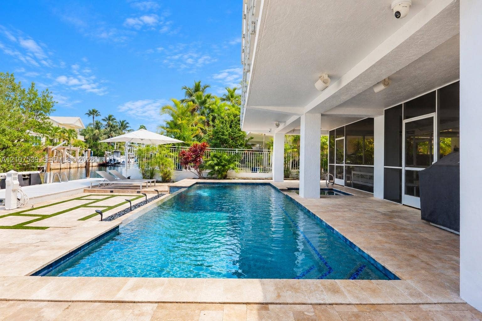 20 Center Lane, Key Largo, FL 33037 In-ground pool with tiled waterline and stone decking, covered patio, integrated spa, and waterfront bulkhead