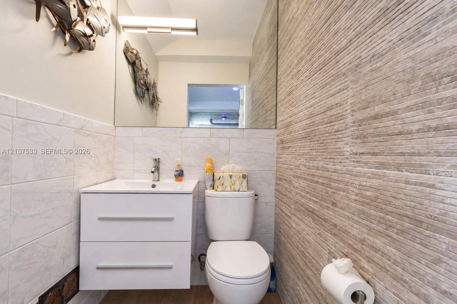 20 Center Lane, Key Largo, FL 33037 Floating white vanity with integrated sink, textured stone-finish accent wall, large format light-colored wall tiling, wall-mounted vanity lighting, and frameless mirror
