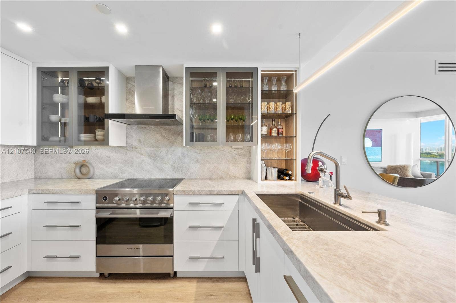 Kitchen featuring custom flat-panel cabinetry, stainless steel Fisher & Paykel gourmet stove with matching hood, built-in glass-front display shelving & an undermount top of the line stainless steel sink with a high-arc faucet