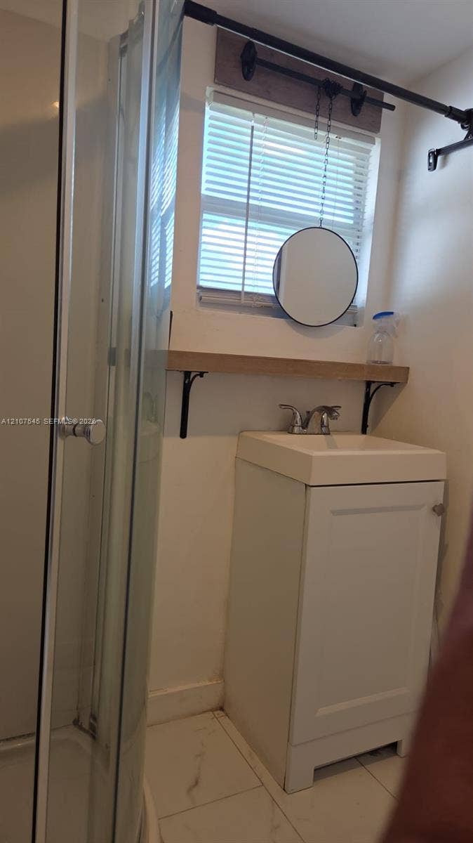 6431 Hayes Street, #3, Hollywood, Hollywood, FL 33024 White vanity featuring a rectangular basin, polished chrome faucet, and integrated wood-tone shelving, complemented by tile flooring and a corner glass-enclosed shower