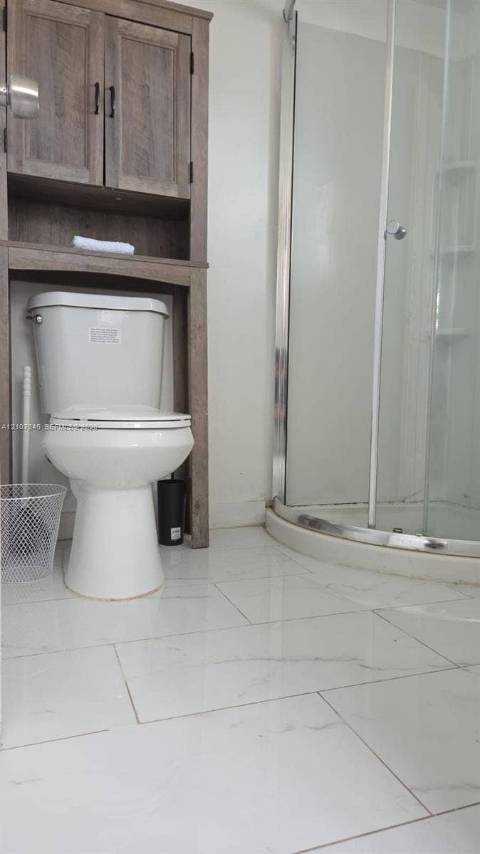 6431 Hayes Street, #3, Hollywood, Hollywood, FL 33024 Curved shower enclosure with glass doors, wood-finish over-the-toilet storage cabinetry, and large-format tile flooring