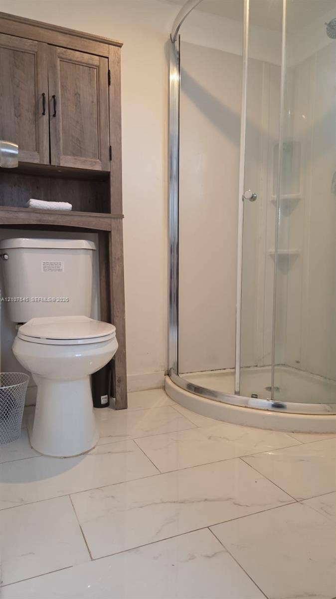 6431 Hayes Street, #3, Hollywood, Hollywood, FL 33024 Curved glass-enclosed shower with integrated shelving, white large-format stone-finish tile flooring, and built-in wood-finish storage cabinetry