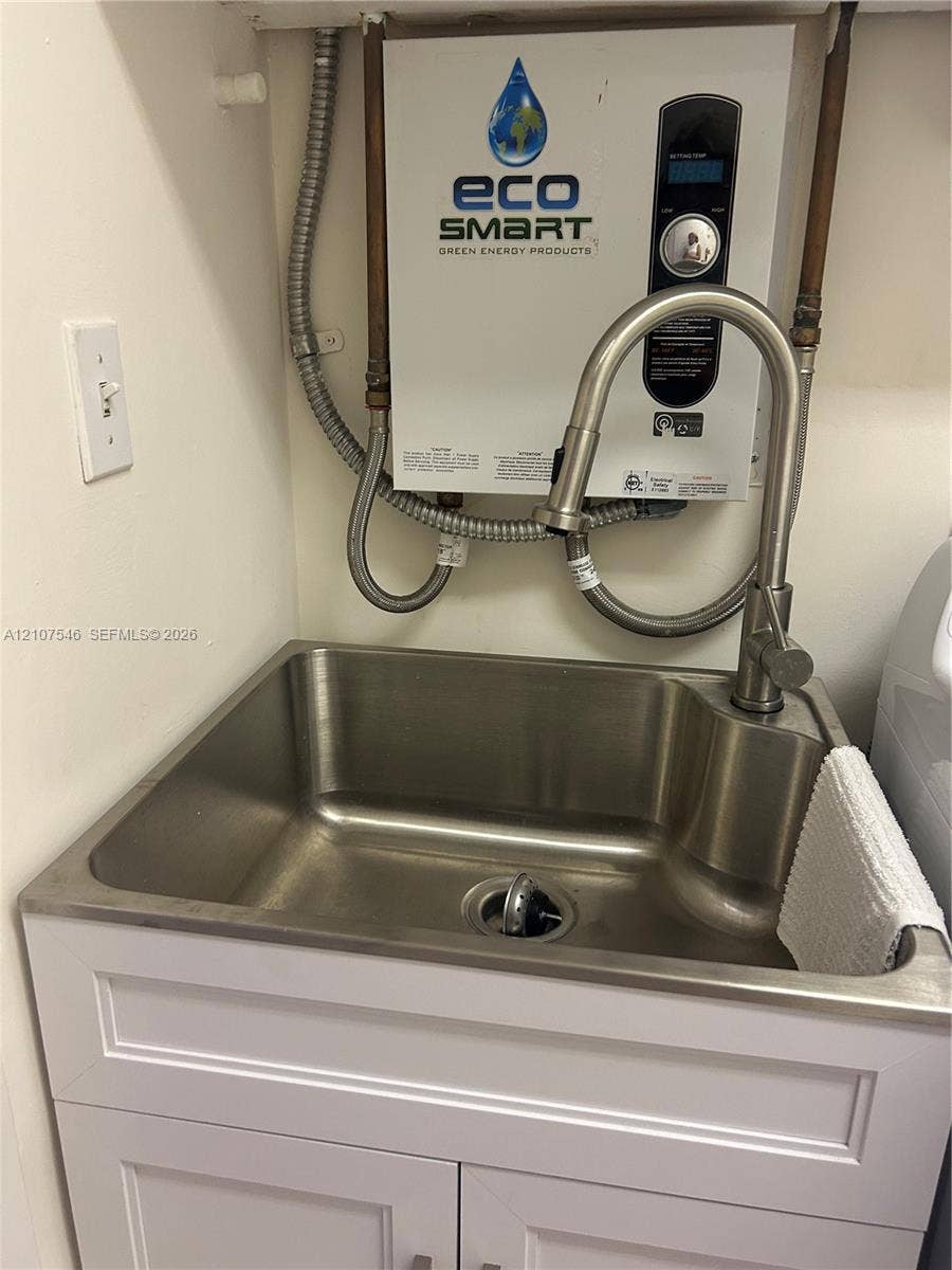 19333 Collins Avenue, #2007, Sunny Isles Beach, Sunny Isles Beach, FL 33160 Stainless steel utility sink featuring a high-arc pull-down faucet, mounted above a white shaker-style vanity cabinet, accompanied by an electric tankless water heater