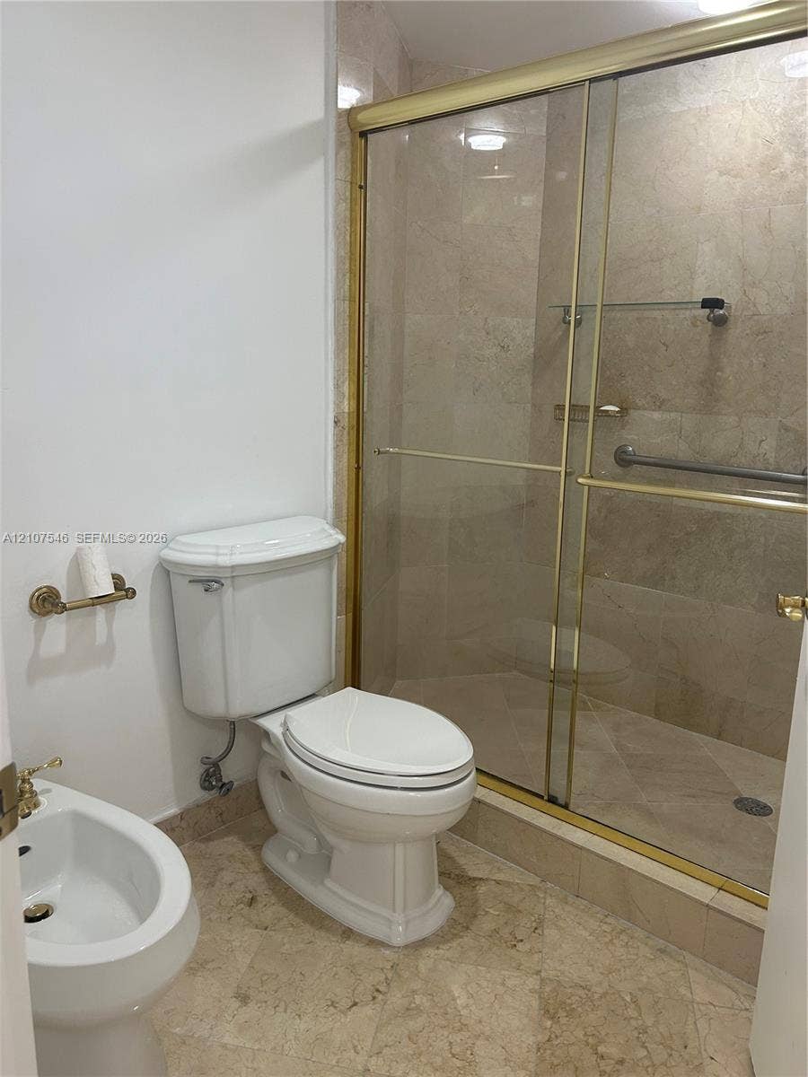 19333 Collins Avenue, #2007, Sunny Isles Beach, Sunny Isles Beach, FL 33160 Bathroom featuring stone tile flooring and shower surround, glass-enclosed shower with metal framing, wall-mounted bidet, and white porcelain toilet