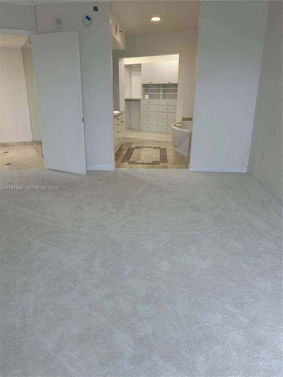 19333 Collins Avenue, #2007, Sunny Isles Beach, Sunny Isles Beach, FL 33160 Carpeted room featuring a custom walk-in closet with built-in cabinetry, drawers, and shelving, stone flooring, and a soaking tub