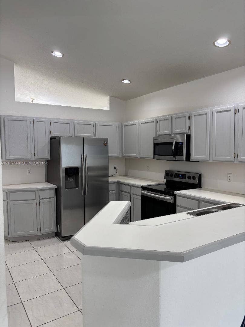 8995 NW 148th Street, #8995, Miami Lakes, Miami Lakes, FL 33018 Kitchen featuring light-toned cabinetry, solid surface countertops, stainless steel appliances, a peninsula counter, and tiled flooring