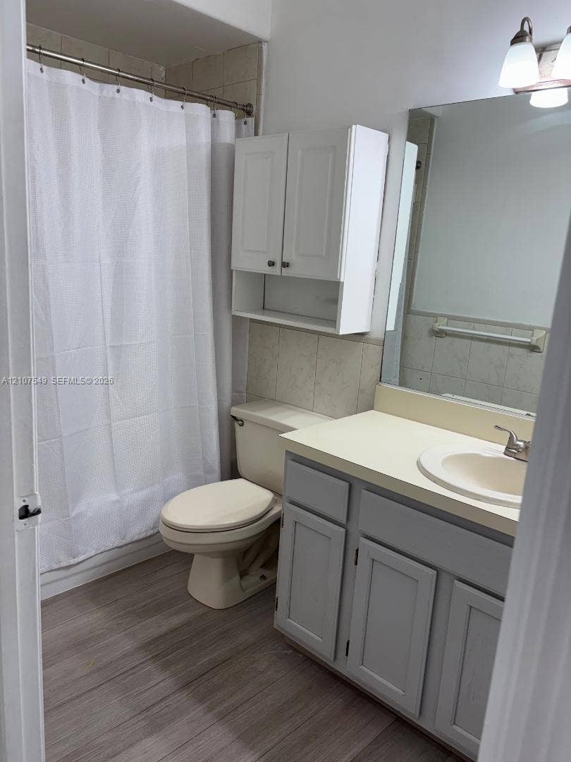 8995 NW 148th Street, #8995, Miami Lakes, Miami Lakes, FL 33018 Bathroom featuring wood-finish flooring, a vanity cabinet with a neutral countertop and integrated sink, wall-mounted storage cabinetry, a large vanity mirror, and a tub-shower combination with tile surround