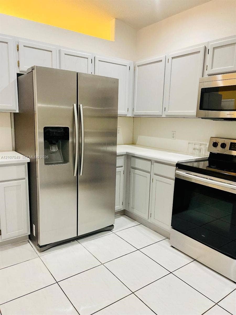 8995 NW 148th Street, #8995, Miami Lakes, Miami Lakes, FL 33018 Kitchen featuring stainless steel side-by-side refrigerator, microwave, and electric range, white cabinetry, solid surface countertops, and ceramic tile flooring