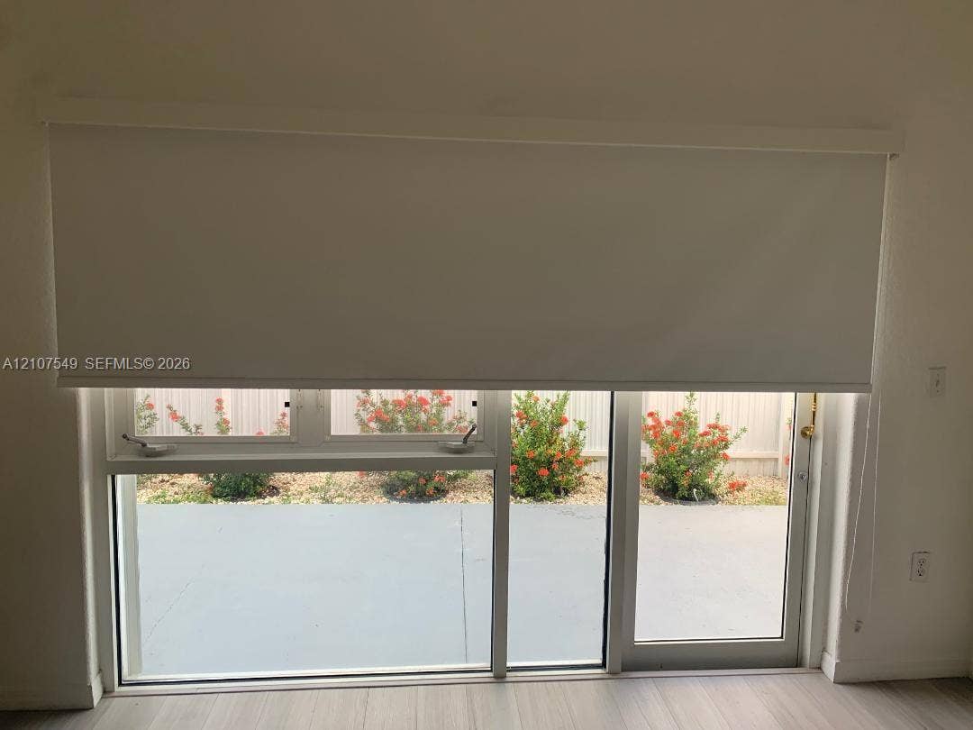 8995 NW 148th Street, #8995, Miami Lakes, Miami Lakes, FL 33018 Large window and sliding glass door combination with white framing, retractable roller shade, and light-toned wood-finish flooring