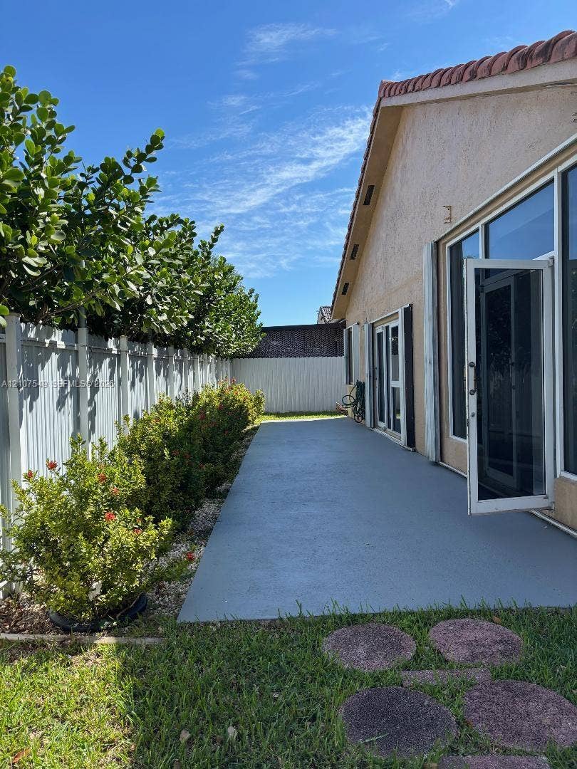 8995 NW 148th Street, #8995, Miami Lakes, Miami Lakes, FL 33018 Exterior patio space featuring a concrete surface, perimeter vinyl fencing, mature hedge landscaping, and oversized glass sliding doors