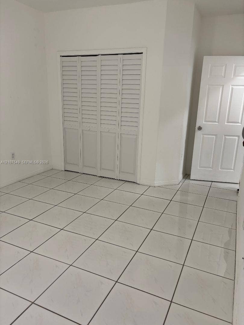 8995 NW 148th Street, #8995, Miami Lakes, Miami Lakes, FL 33018 Large-format white tile flooring, four-panel interior door with brushed metal hardware, and bi-fold louvered closet doors