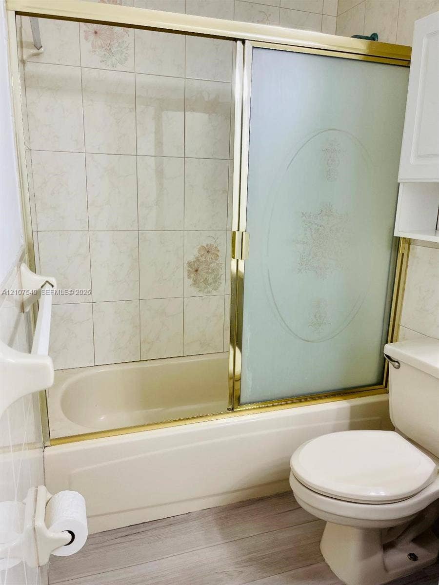 8995 NW 148th Street, #8995, Miami Lakes, Miami Lakes, FL 33018 Bathtub with gold-tone frame sliding glass enclosure, decorative tile surround, standard-height toilet, and built-in white wall cabinetry