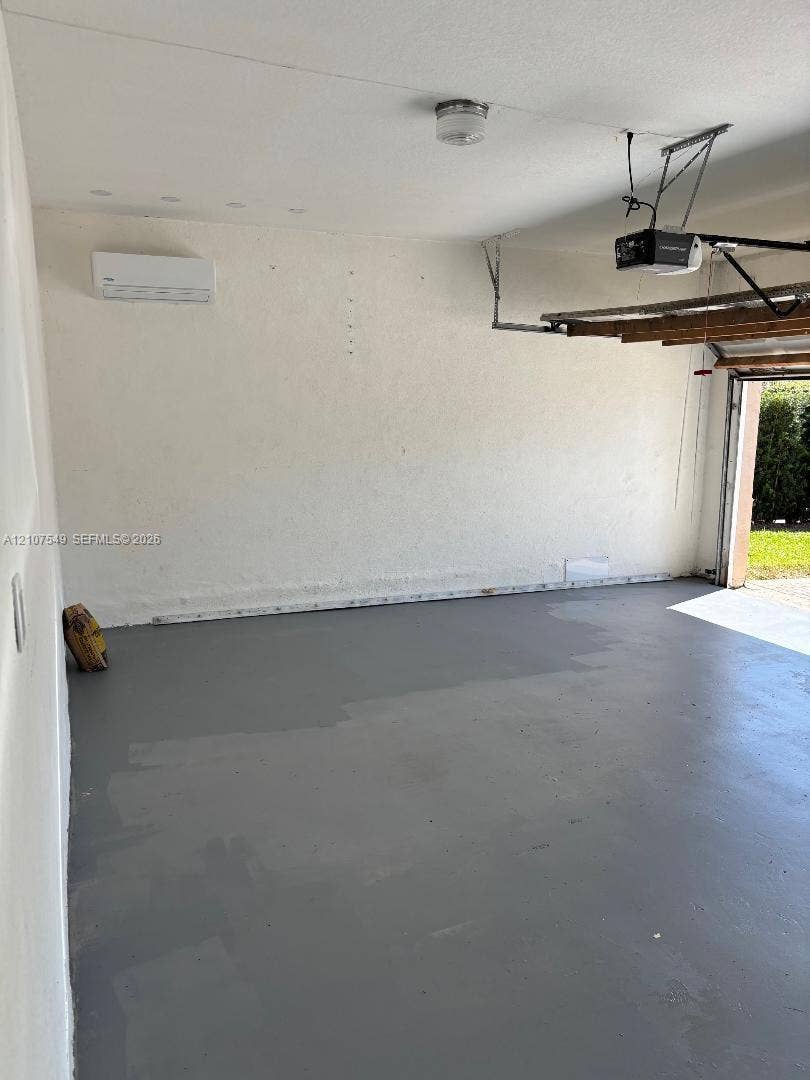 8995 NW 148th Street, #8995, Miami Lakes, Miami Lakes, FL 33018 Garage space featuring finished gray flooring, wall-mounted ductless climate control unit, and overhead garage door opener